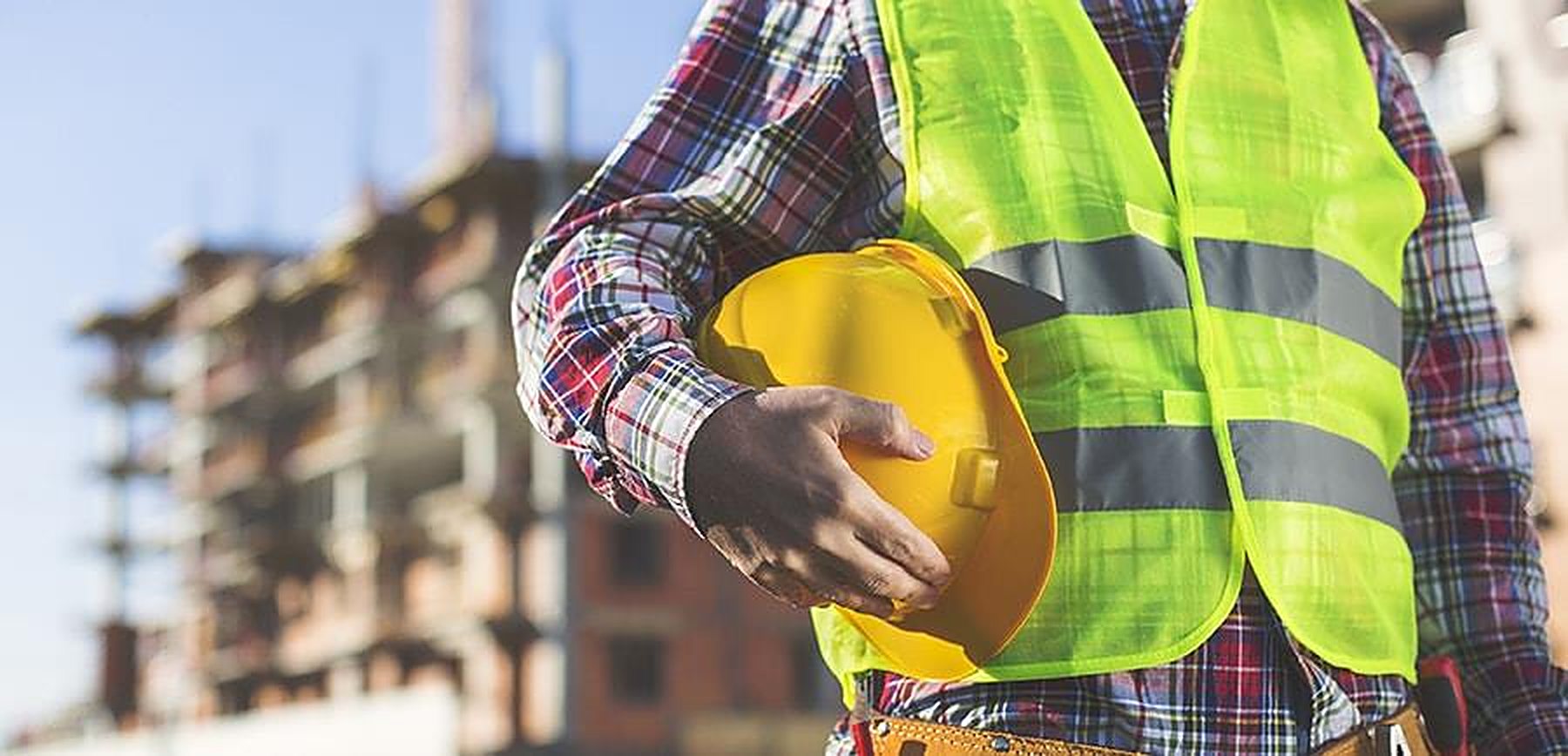 Site worker in a hi-vis vest holding a yellow hard hat